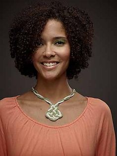 a woman with curly hair wearing a necklace and an orange top smiling at the camera