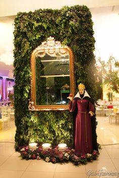 a woman standing in front of a mirror surrounded by greenery and flowers on display