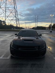 a black car parked in a parking lot next to power lines and telephone poles on a cloudy day