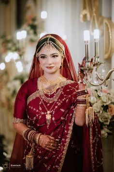 a woman in a red and gold bridal outfit holding a candelabra