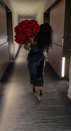 a woman walking down a hallway holding a bunch of red roses