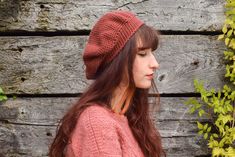 a woman wearing a red hat standing next to a wooden wall with ivy growing on it