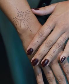 two hands holding each other with sunburst tattoos on their fingers and wristbands