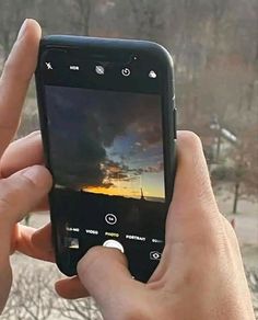 someone holding up their cell phone to take a photo with the sky in the background