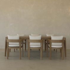 a wooden table with six chairs and white pillows on top of it in front of a beige wall