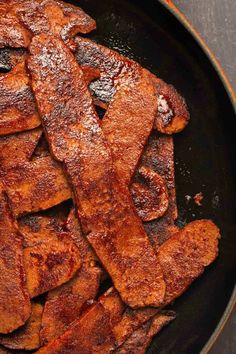 bacon is cooking in a frying pan on the table