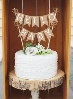 a white cake sitting on top of a wooden table next to a sign that says hello baby