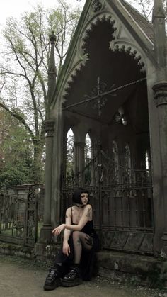 a woman sitting on the ground in front of a building with an iron fence around it