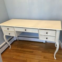 a white desk with two drawers in a corner next to a wall and hardwood floor