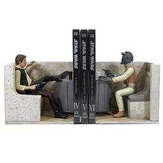 two figurines sitting on a bench next to each other in front of three books