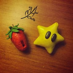 two small plastic toys sitting on top of a wooden table next to a star and a strawberry