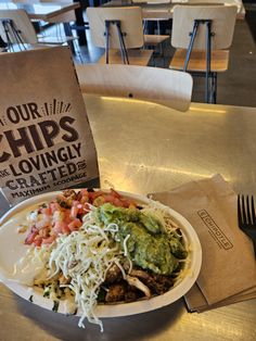 a white plate topped with meat and veggies next to a bag of chips