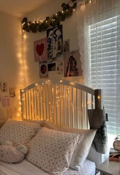 a white bed topped with lots of pillows next to a window covered in fairy lights