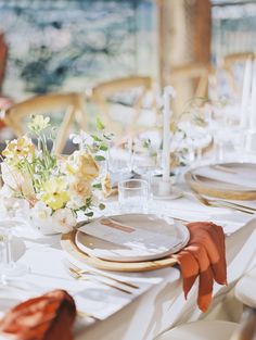 the table is set with white and gold plates, napkins, and flower centerpieces