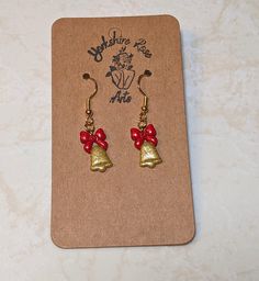 Introducing our elegant Golden Bells Earrings - a breathtaking fusion of sophistication and festive charm. Crafted from polymer clay, these earrings exude the opulent beauty of sparkling gold bells adorned with vibrant red ribbons, creating a statement accessory that embodies the spirit of the season. Each bell is meticulously detailed to capture the richness and shimmer of real gold, ensuring you radiate elegance at every holiday gathering. The festive red ribbons delicately tied on top add a t Gold Holiday Drop Earrings, Red Jewelry For Christmas Celebration, Red Earrings For Christmas Gift, Holiday Red Adjustable Jewelry, Red Jewelry For New Year Holiday, Gold Earrings For Holiday And New Year, Handmade Red Jewelry For New Year, Gold Dangle Earrings For Holiday, Elegant Christmas Celebration Earrings