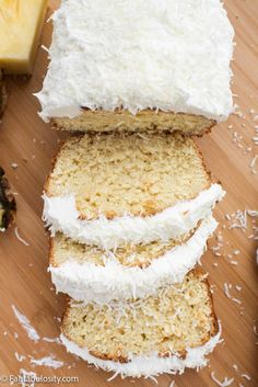 slices of cake with white frosting sitting on top of a wooden cutting board next to sliced pineapples