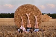 two people laying on the ground in front of a hay bale with their hands up