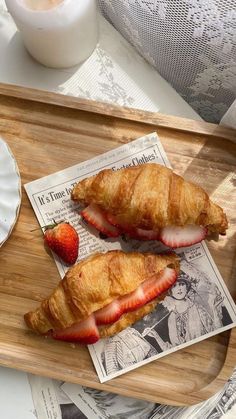 two croissants with strawberries are on a wooden tray