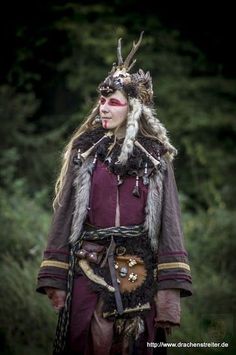 a woman wearing a costume with horns and feathers on her head is standing in the woods