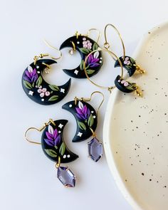 four pairs of earrings with flowers and leaves painted on them sitting next to a plate