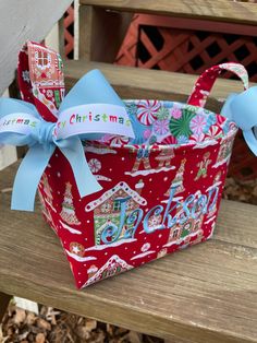 a red christmas gift bag with blue ribbon on a wooden bench in front of a house