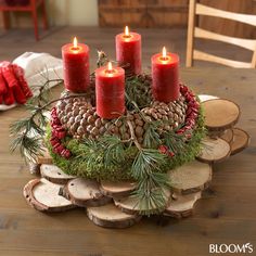 a candle holder with pine cones, evergreen and red candles on it sitting on a wooden table