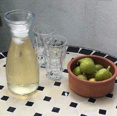 a bowl of green olives next to two glasses and a bottle on a table