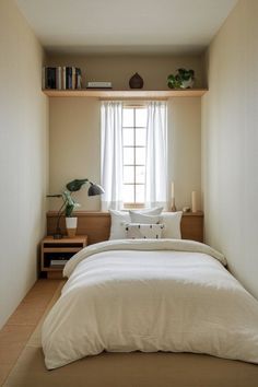 a bed sitting under a window next to a wooden shelf filled with books and plants