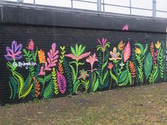 a wall painted with colorful flowers and plants on it's side near a parking lot