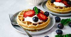 two waffles with strawberries and blueberries on top, one is topped with whipped cream