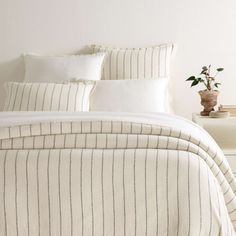 a bed with white and black striped comforter next to a plant on a nightstand