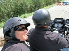 two people riding on the back of a motorcycle down a curvy road with trees in the background