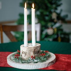 three white candles sitting on top of a wooden plate with holly and red berries around it