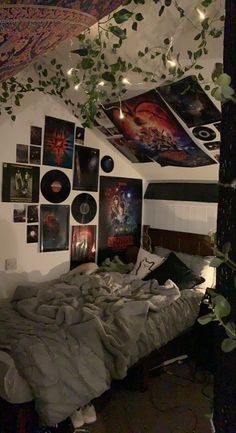 an unmade bed in a room with pictures on the wall and plants hanging from the ceiling