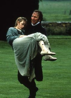 the man is carrying the woman on his back in an open field with green grass