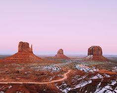 the desert is covered in snow and red rock formations at dusk, with a pink sky