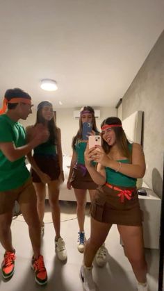 group of people taking selfies with cell phones in an apartment hallway, one woman wearing green shirt and brown skirt