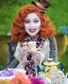 a woman with red hair and makeup is holding a tea cup in front of her face