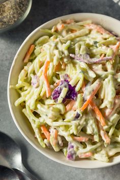 a white bowl filled with coleslaw salad next to silverware and spoons