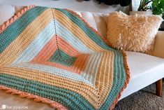 a crocheted blanket sitting on top of a white couch next to a pillow