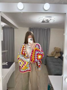 a woman is taking a selfie in the mirror with her cell phone and wearing a crocheted jacket