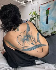 a woman with a tattoo on her back sitting on a bed next to a parrot