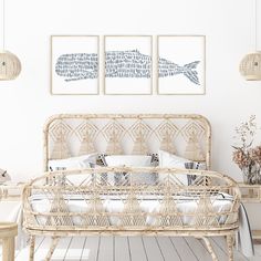 a wicker bed with white sheets and pillows in a room that has two paintings on the wall