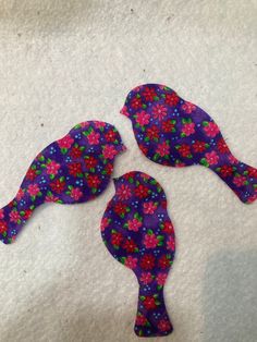 three birds made out of fabric sitting on top of a white sheet with pink and blue flowers