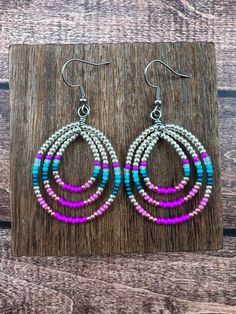 the multicolored beaded hoop earrings are displayed on a wooden board with wood planks