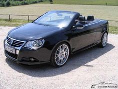 a black convertible car parked on top of a gravel road next to a fence and field