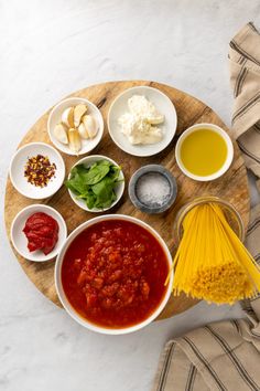 the ingredients to make this pasta dish are arranged on a wooden platter, along with bowls of sauces and seasonings