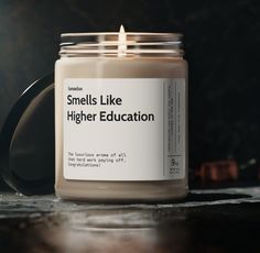 a candle sitting on top of a table next to a black container with the words smells like higher education written on it