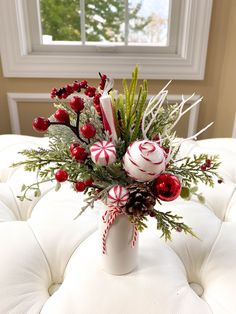 a vase filled with candy canes and greenery on top of a white ottoman