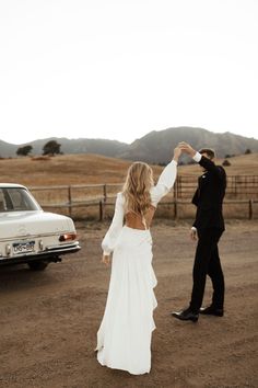 a bride and groom standing in the middle of a dirt road with their arms around each other